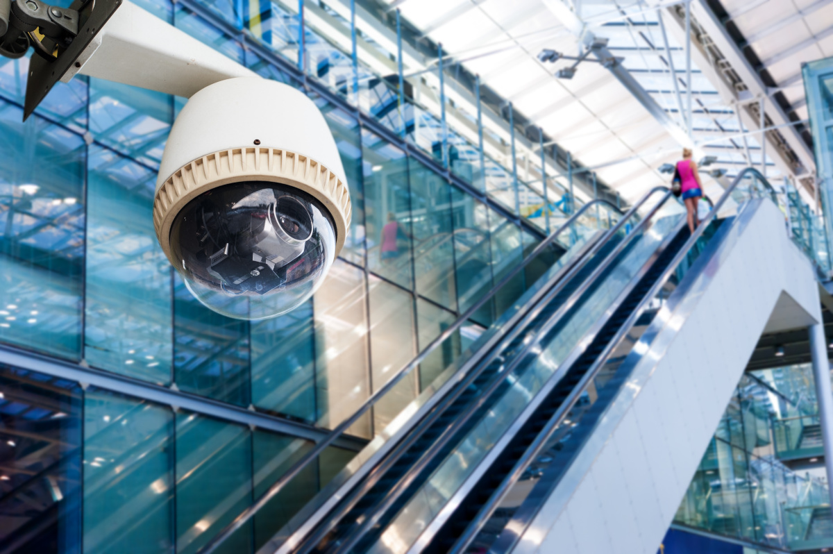 Close Up of Surveillance Camera with Woman on Escalator in Background
